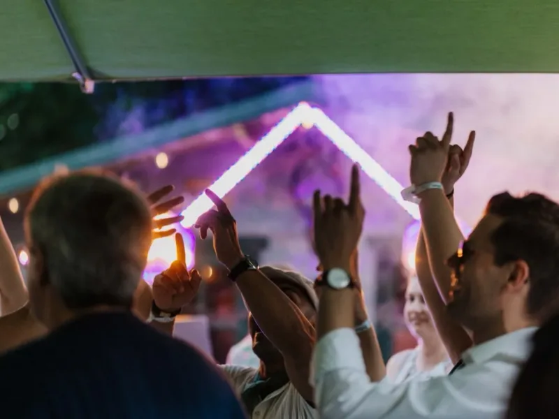 Feiergäste mit erhobenen Händen bei einer Party unter dem Sonnensegel im Haus Pöpsel.